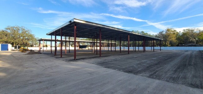 A wide angle photo of covered parking meant for cars. The cover is a flat roofed structure comprised of red beams